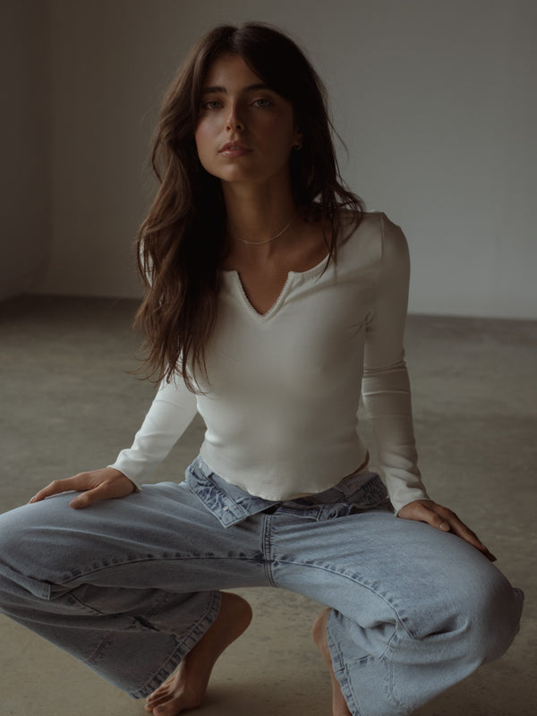 Modelo usando top manga larga crudo y jean azul bota ancha.