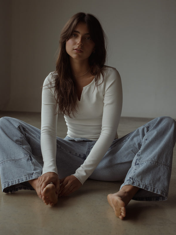 Modelo sentada usando jean azul ancho con top crudo manga larga.