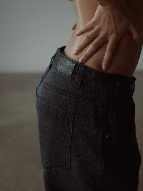 Vista lateral a detalle de garra, bolsillos y pretina de jean negro azul.