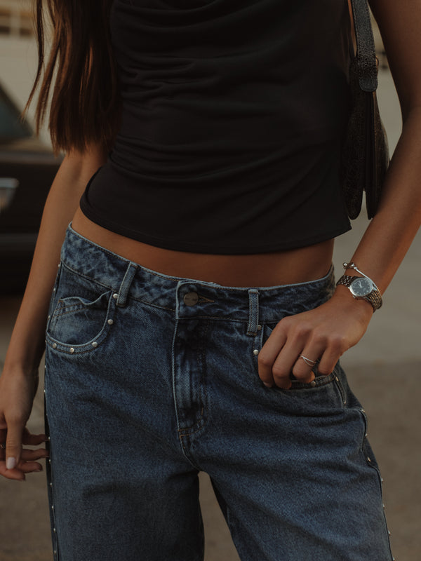 Vista frontal de pretina de jean azul con apliques metálicos y top negro.