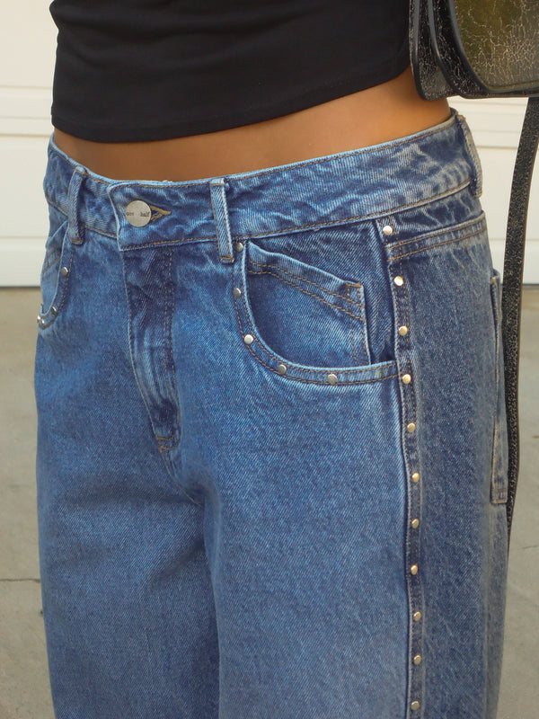 Vista frontal jean azul con apliques metálicos laterales.