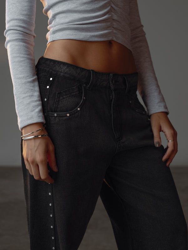 Vista lateral modelo con jean gris claro y oscuro con apliques metálicos.