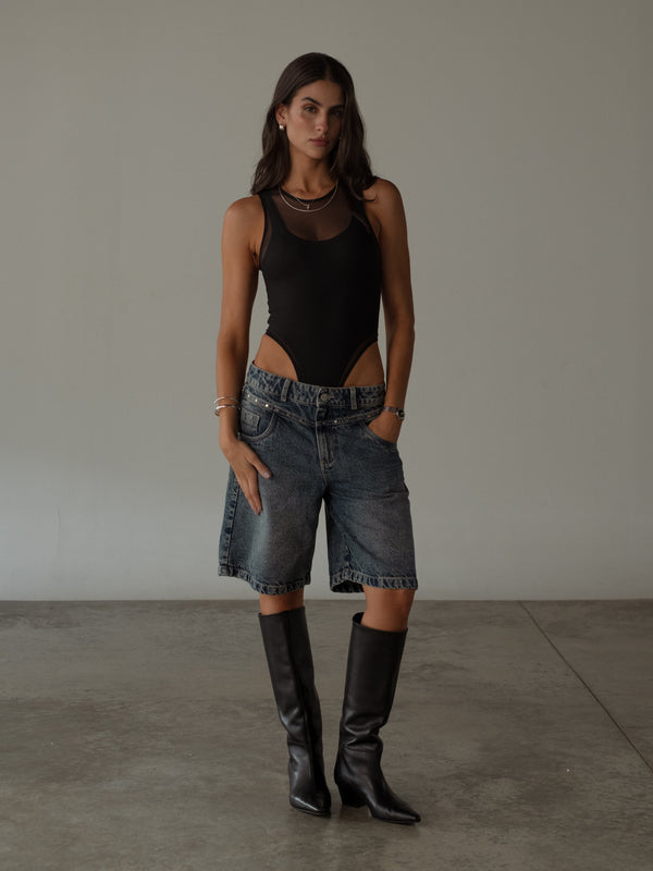 Modelo con short azul con detalles metálicos con bodie negro y botas.