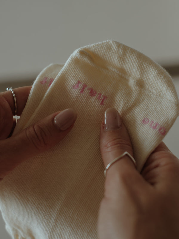 Vista a detalle punta de medias crema con bordado rosa "One Half".
