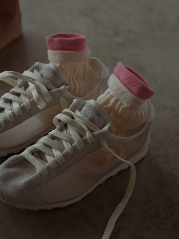 Medias crema con borde rosa dentro de tenis gris.