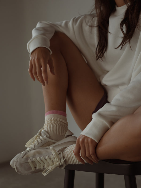 Modelo sentada usando medias crema con rosa y ropa deportiva.