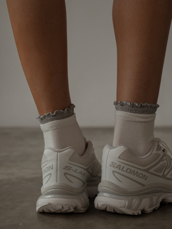 Vista posterior medias blancas con borde gris brillante y tenis blancos.