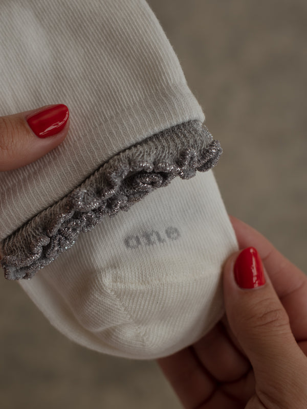 Vista a detalle de borde ruche gris brillante de medias blancas.