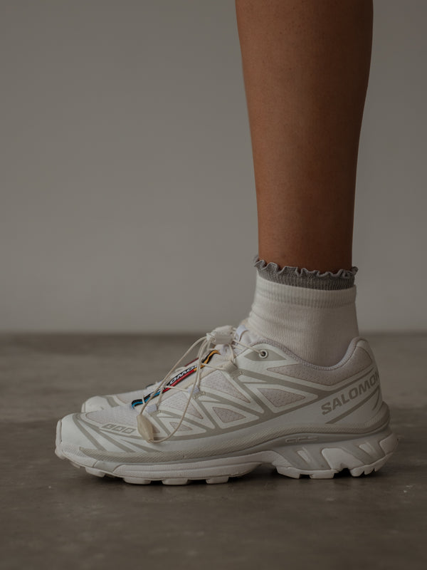 Vista lateral de tenis blancos con medias midi con borde brillante gris.