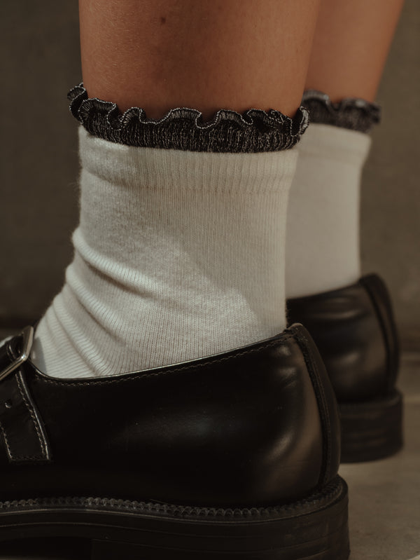 Vista a detalle de borde negro brillante de medias midi blancas.