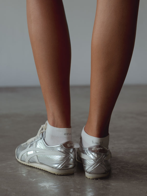 Vista posterior medias tobilleras blancas con bordado gris “One Half” en puño. 