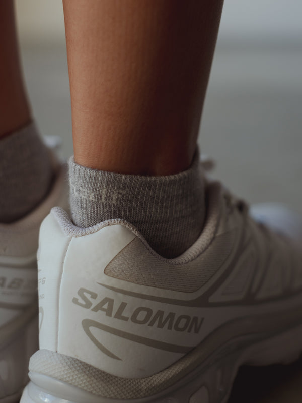 Vista a detalle puño de medias grises tobilleras con tenis blancos. 