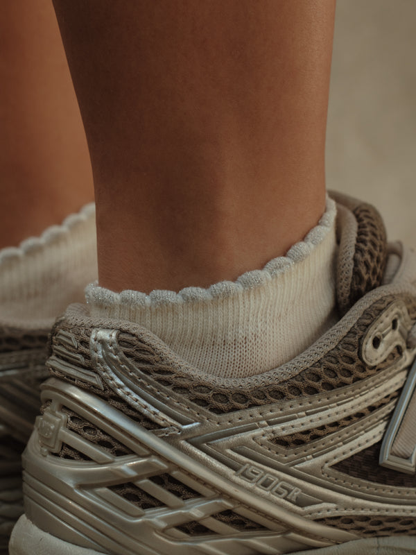 Vista lateral a detalle borde gris brillante de medias tobilleras crema.