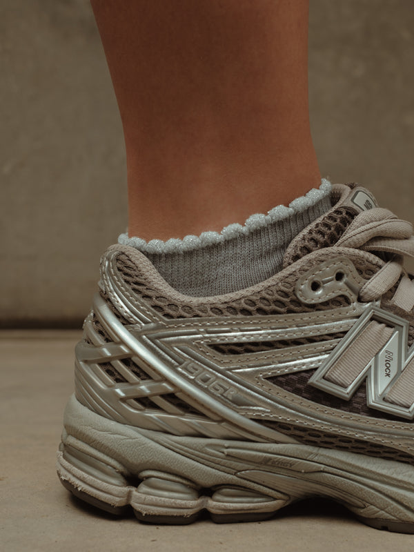 Vista lateral de medias grises tobilleras con borde brillante y tenis.