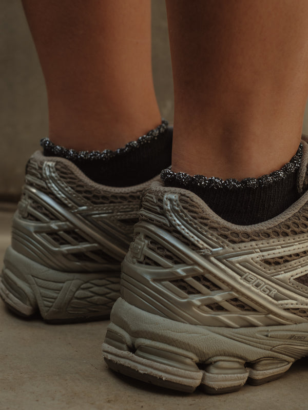 Vista posterior de medias tobilleras negras de borde brillante con tenis.