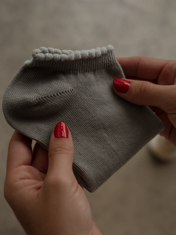 Vista frontal de media tobillera gris doblada con borde brillante.