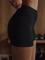 Vista lateral modelo usando mini short deportivo negro pretina curva.