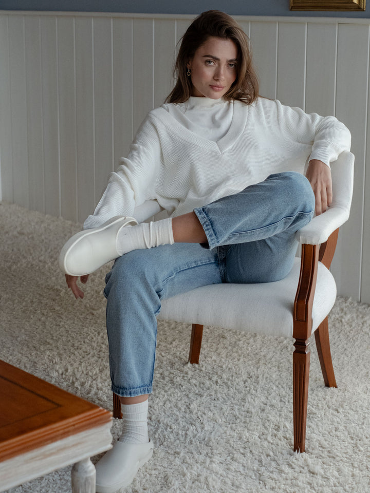 Modelo usando un suéter blanco con un jean bota recta con ruedo al corte a la altura del tobillo