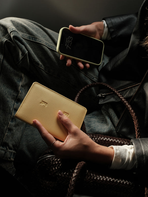 Modelo en avión sosteniendo porta pasaporte amarillo y celular.