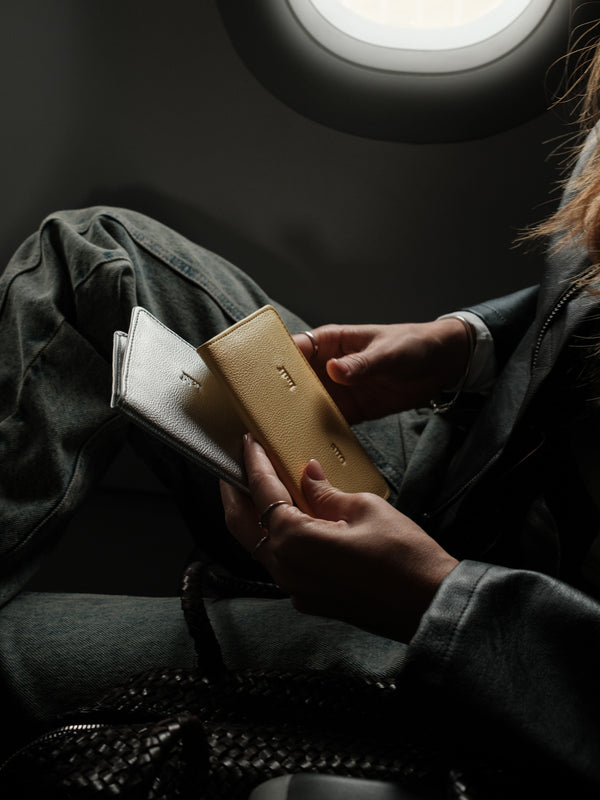 Modelo con dos porta pasaporte amarillo y plata en la mano.