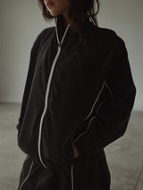 Modelo usando chaqueta rompe vientos negra con líneas en crudo.