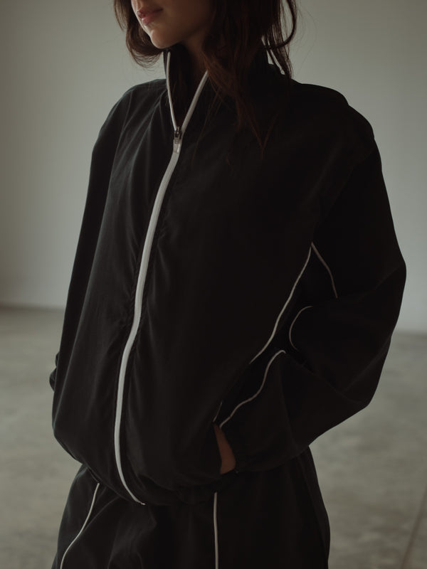 Modelo usando chaqueta rompe vientos negra con líneas en crudo.