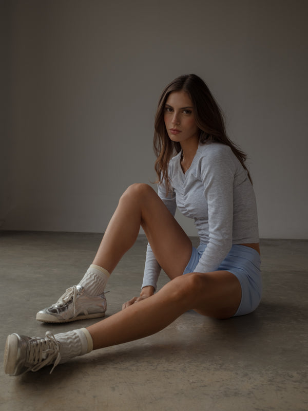Modelo sentada en el piso usando jersey gris con short deportivo azul.