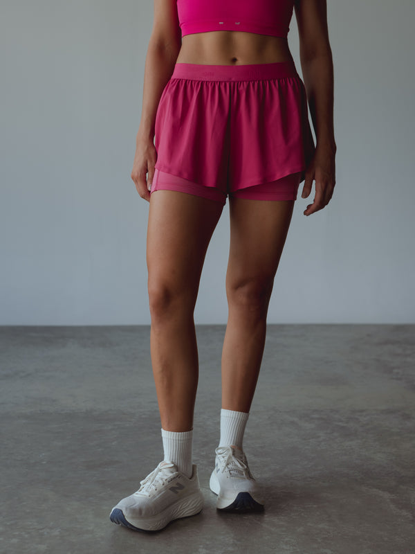 Vista frontal short deportivo fucsia con medias midi blancas y tenis.
