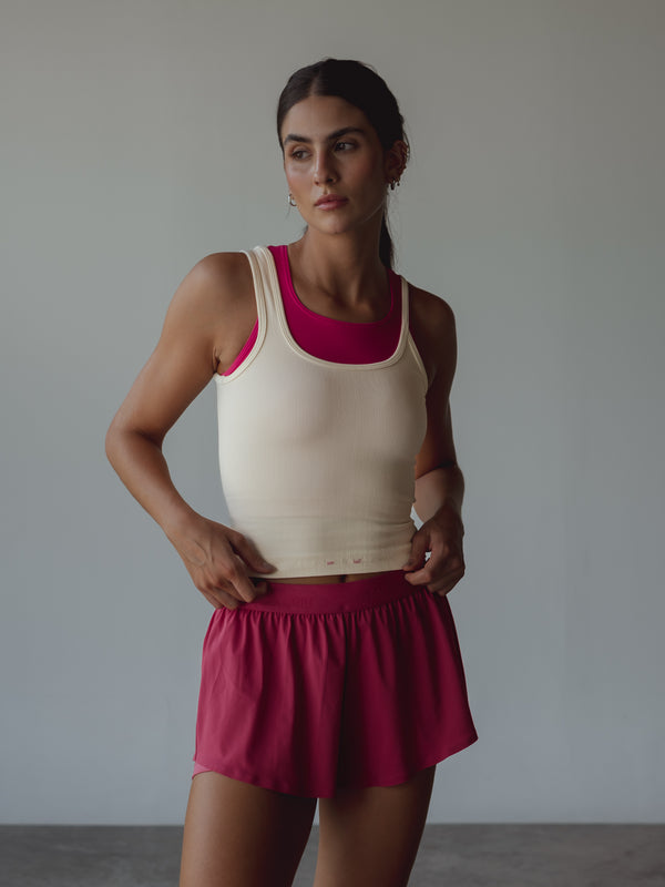 Modelo usando tank crema, top interno fucsia y shorts deportivos del mismo color.
