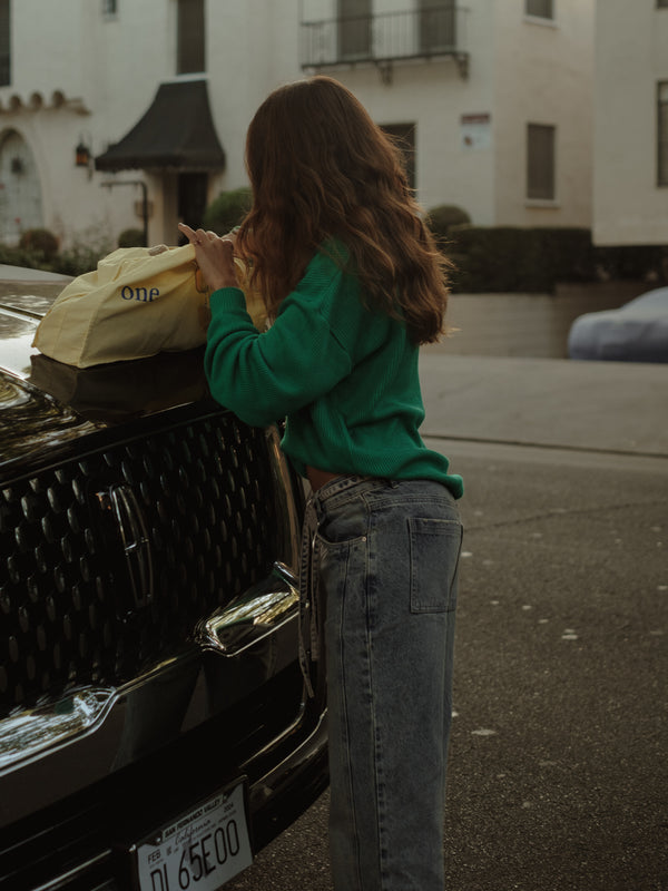 Modelo usando suéter tejido verde y jean buscando en tote bag amarilla.