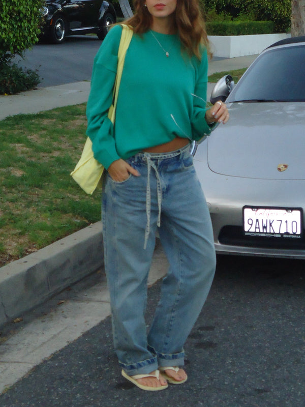 Modelo en la calle usando suéter verde tejido con jean, sandalias y tote bag.