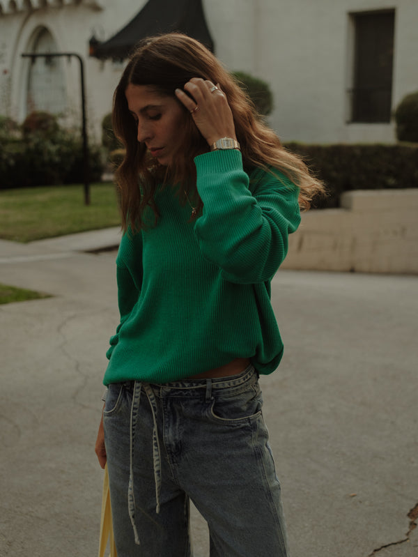 Modelo en la calle usando jean y suéter tejido verde.