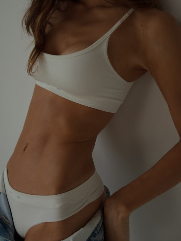 Vista frontal de modelo usando top y tanga crudo con jean.