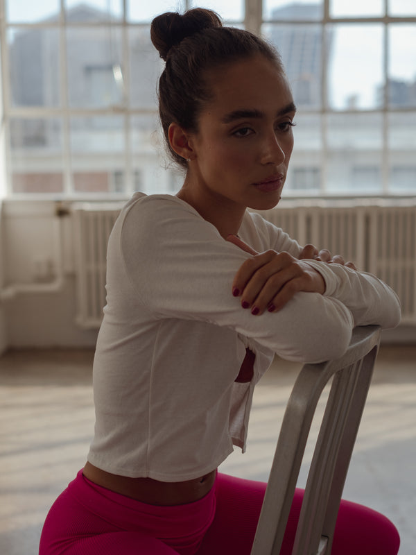 Modelo sentada con vista lateral de top crema escotado con nudo al frente.