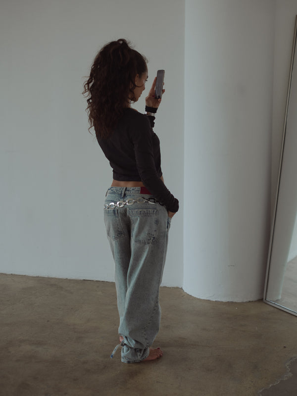 Modelo de espalda mirando el celular con top negro manga larga y jean.