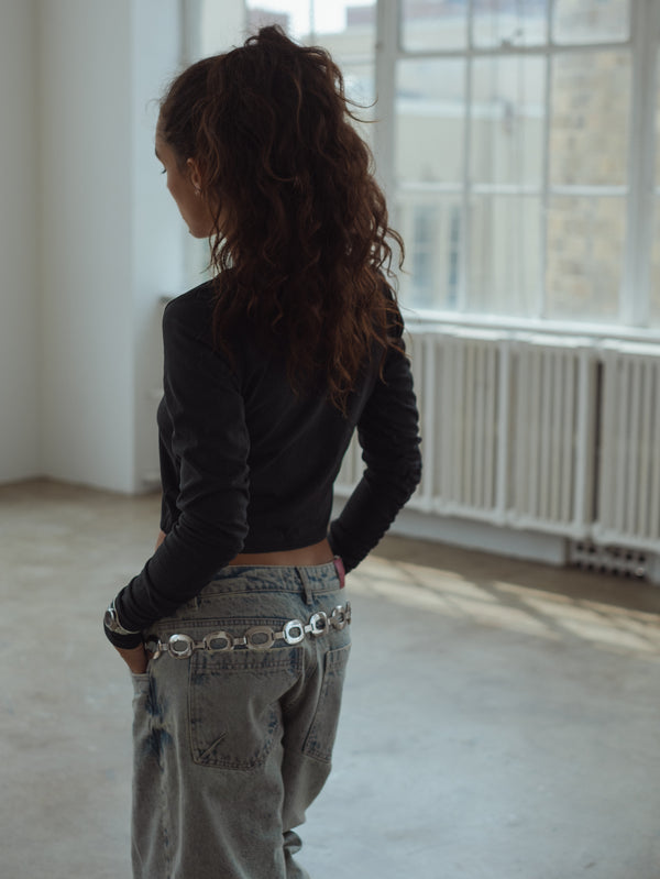 Modelo de espalda con las manos en los bolsillos con top negro manga larga.
