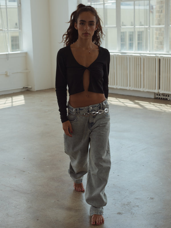 Modelo caminando descalza mientras viste jean claro y top de nudo negro.