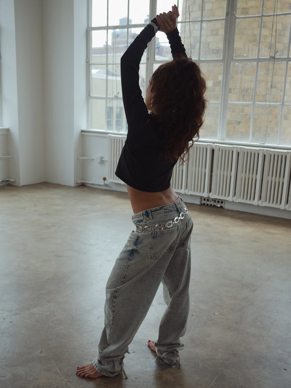 Modelo de espalda con los brazos arriba usando jean ancho con top de nudo negro.