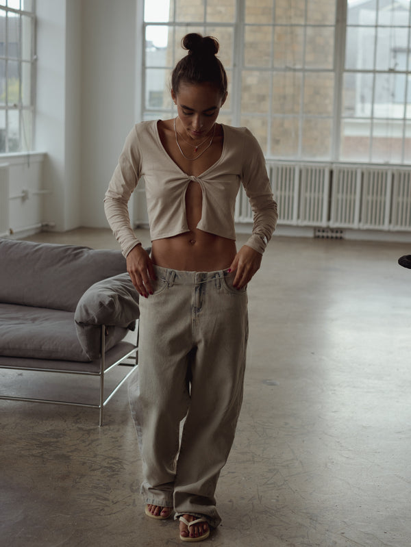 Modelo de frente usando jean ancho, sandalias y top de nudo taupe.