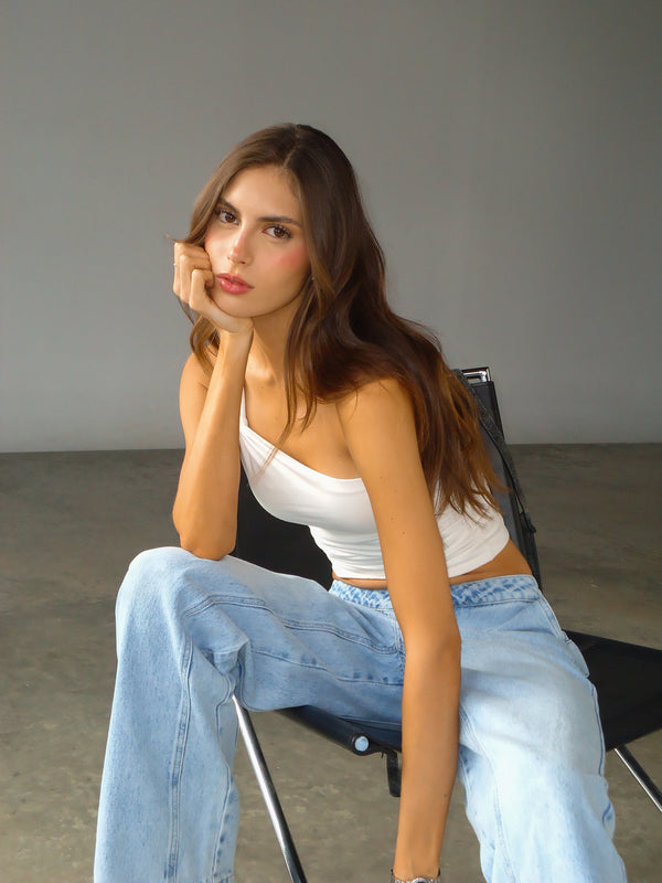 Modelo sentada usando crop top de un hombro crudo y jean azul claro.