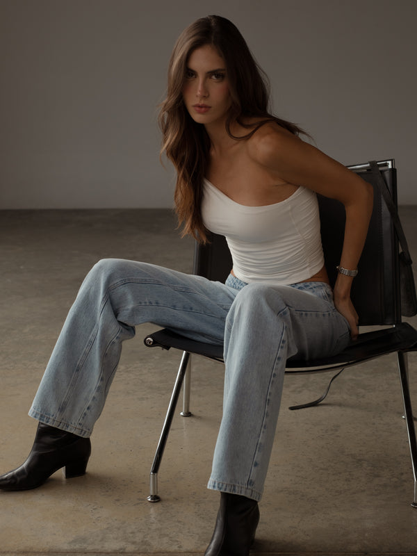 Modelo usando crop top crudo ajustado con jean azul y botas negras.