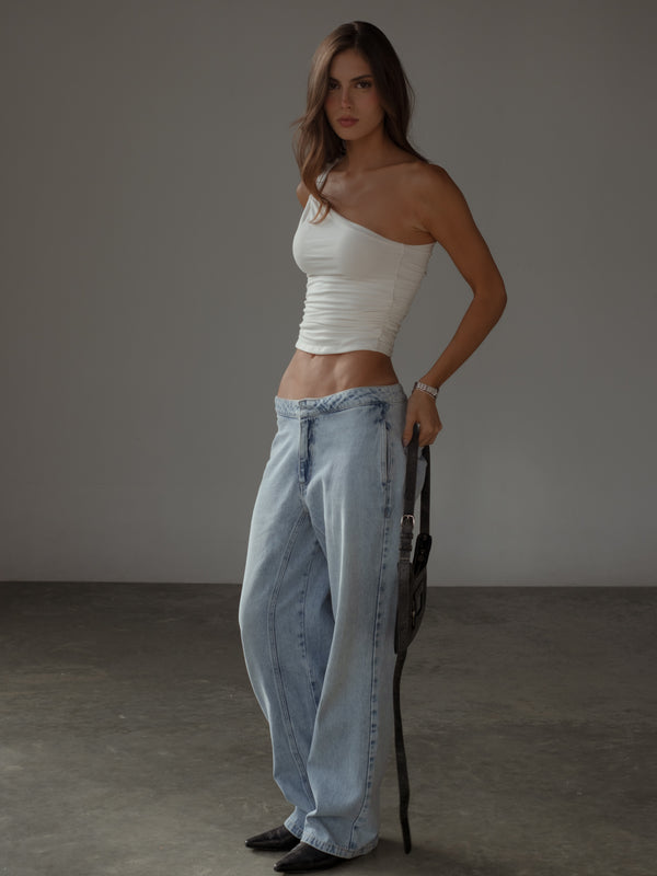 Modelo usando crop top de un hombro drapeado crudo y jean.