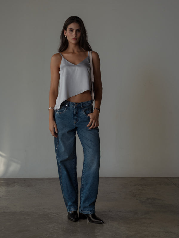 Modelo usando top satinado plata de tiras con jean y botas.