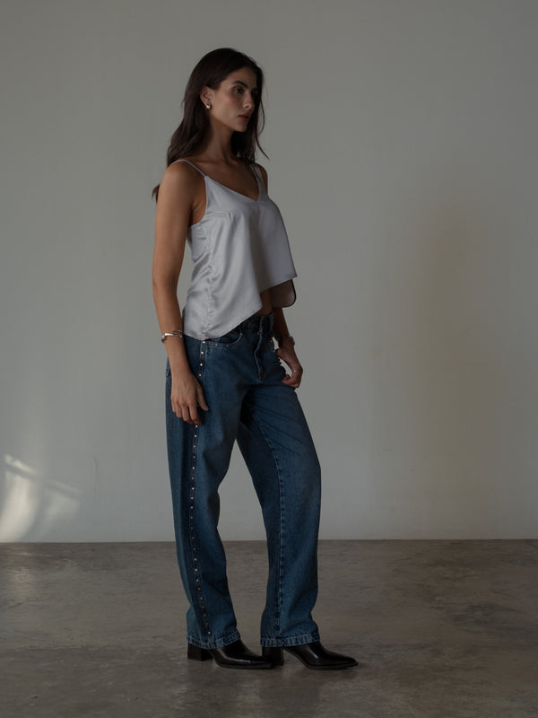 Vista lateral modelo usando jean azul con top satinado plata y botas.