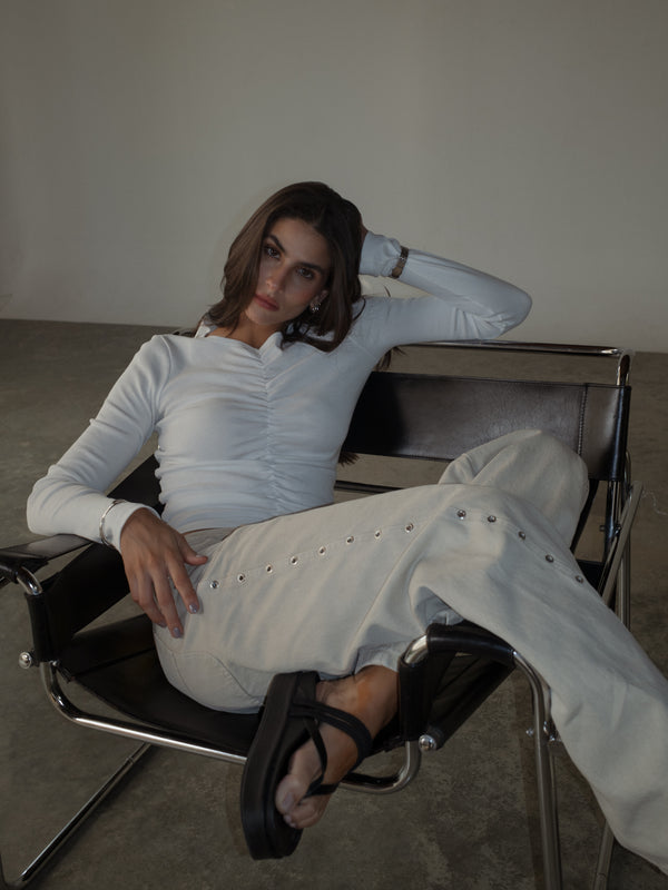 Modelo sentada usando jean crema y top manga larga crudo recogido.