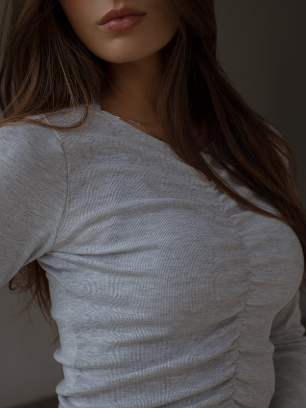 Vista frontal a detalle recogido de top manga larga gris.