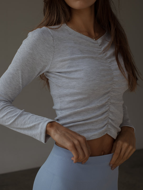 Modelo con top manga larga gris de recogido en medio efecto drapeado.