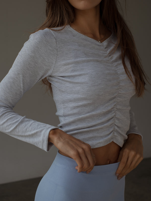 Modelo con top manga larga gris de recogido en medio efecto drapeado.