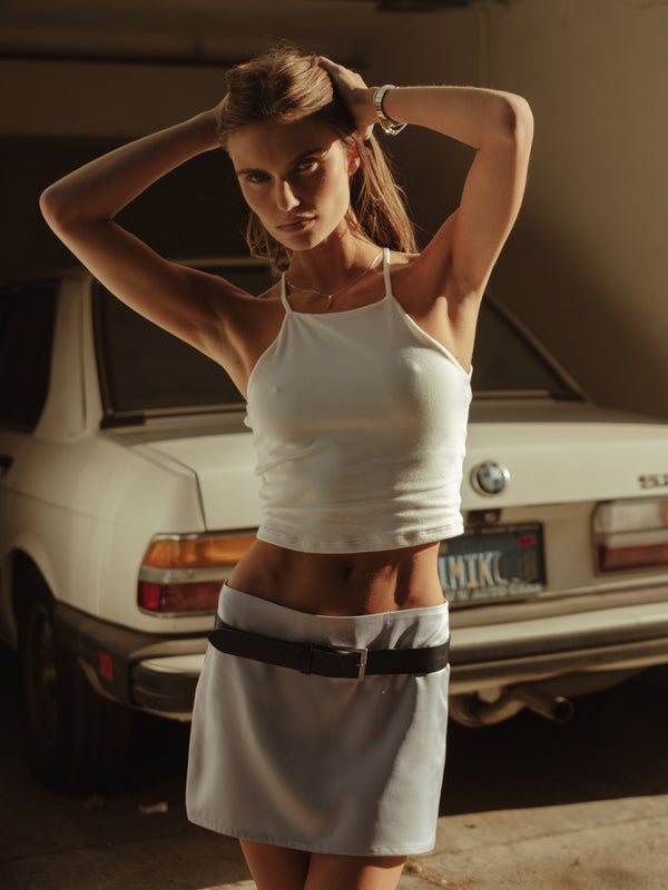 Modelo usando crop top halter crudo con mini falda satín con cinturón.