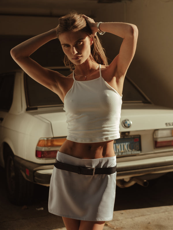 Modelo usando crop top halter crudo con mini falda satín con cinturón.